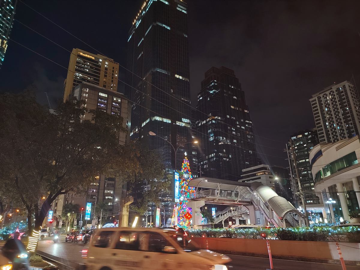 Office towers and a pedestrian footbridge in Pasig City at night, with holiday lights along the road
